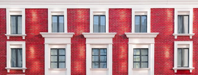 Teilansicht zeigt 2 Reihen à 4 Fenstern eines Altbau-Stadthauses mit roter Backsteinfassade und weißen Stuckeinfassungen der Fenster.